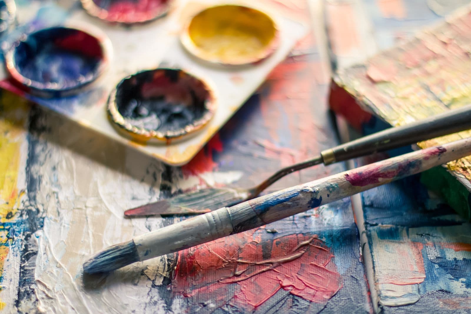 Paintbrushes and a palette knife resting on a colourful oil-painted canvas in an artist's studio