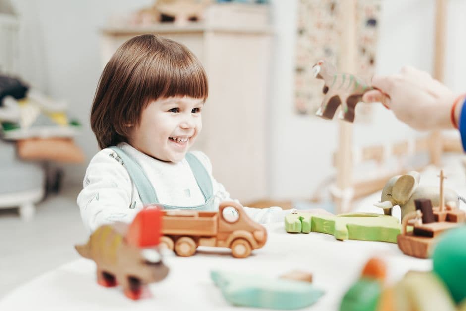 Registered childminder sitting on the floor of a home playroom with wooden toys and two young children