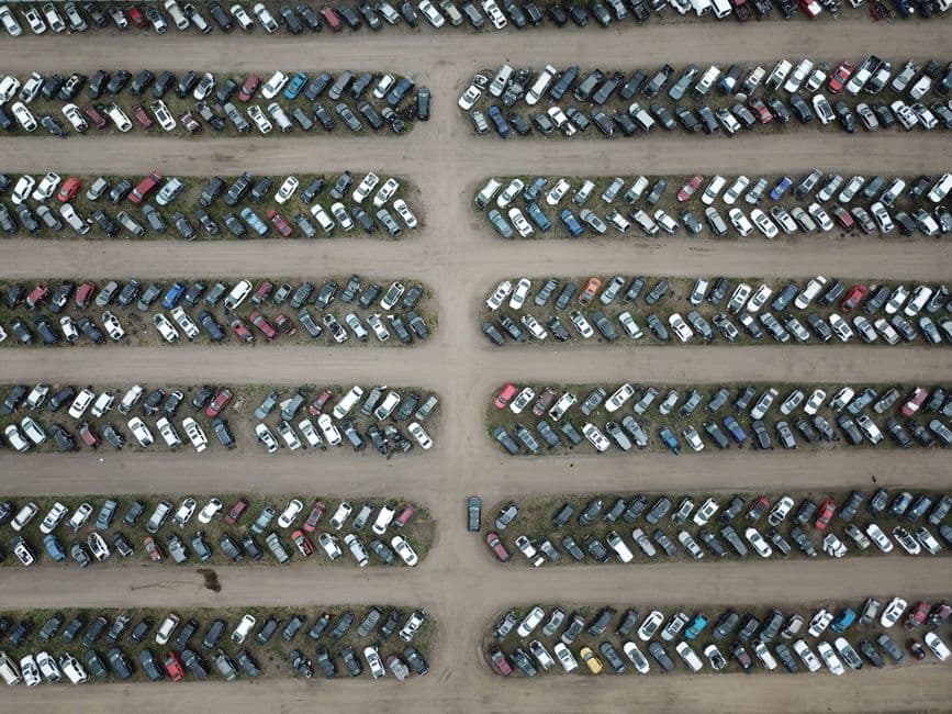 Row of used cars parked on an independent dealership forecourt with a workshop building behind