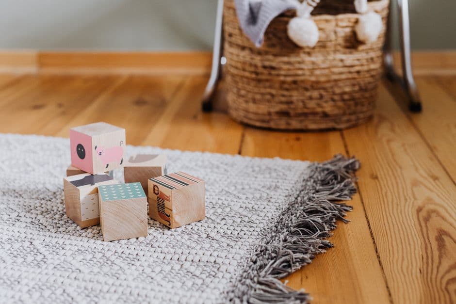 Wooden building blocks, a stacking toy and picture books on a rug in a home childminding setting