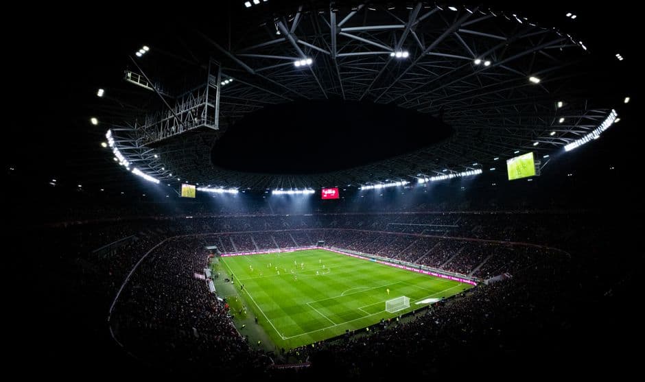 Empty floodlit football stadium seen from the halfway line at dusk