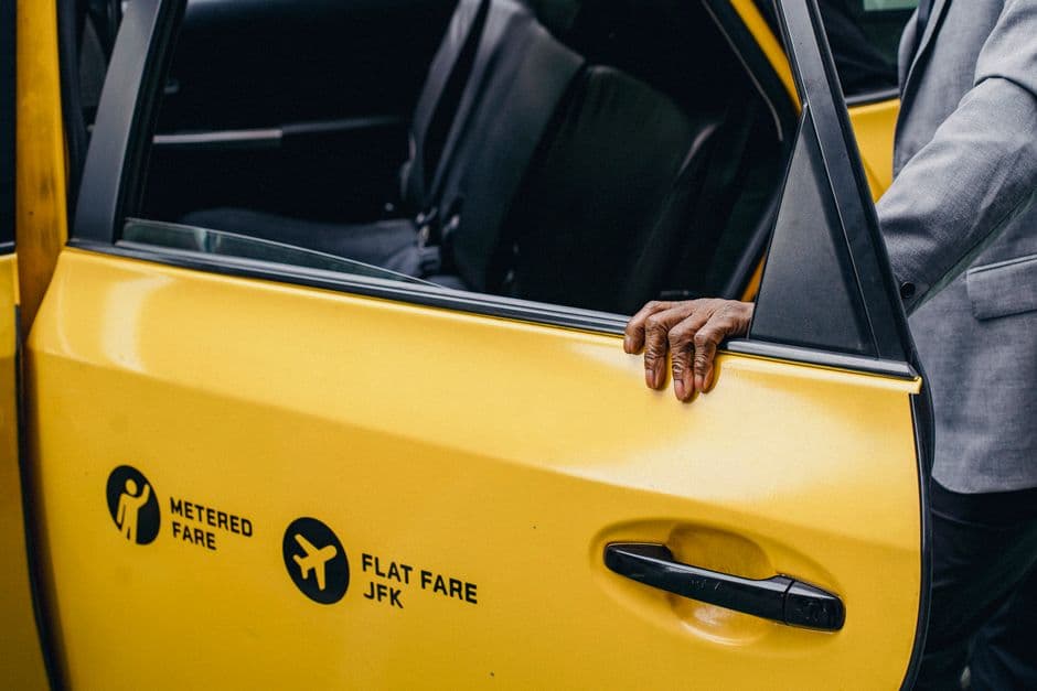 A licensed black taxi and a private hire car waiting at a city rank at dusk with the meter visible through the windscreen