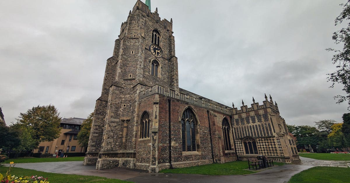A low-angle view of Chelmsford Cathedral with its clock tower and stained glass windows under a cloudy sky.