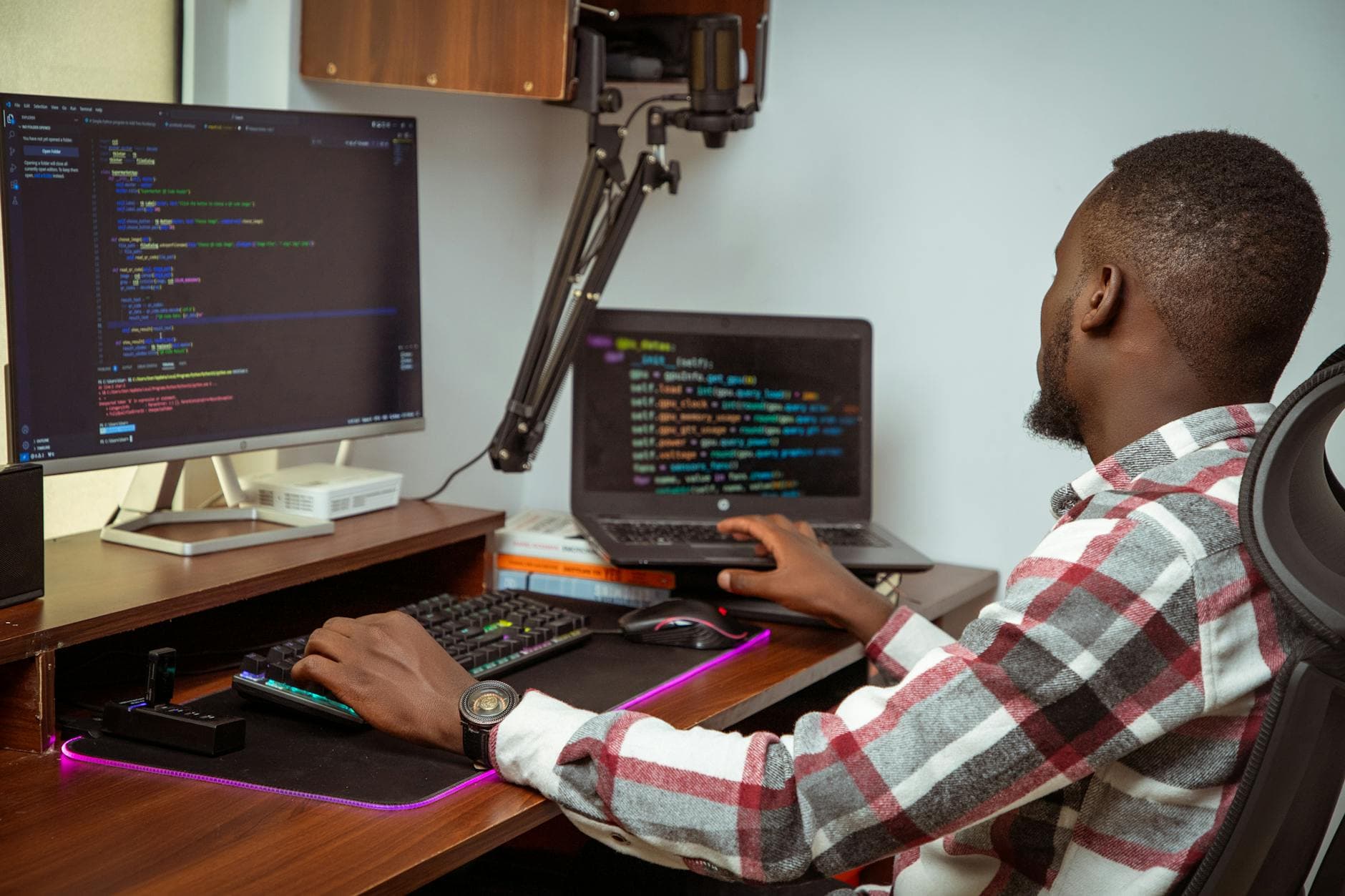 Software developer working on code at a desk in a modern UK office with dual monitors and notebooks