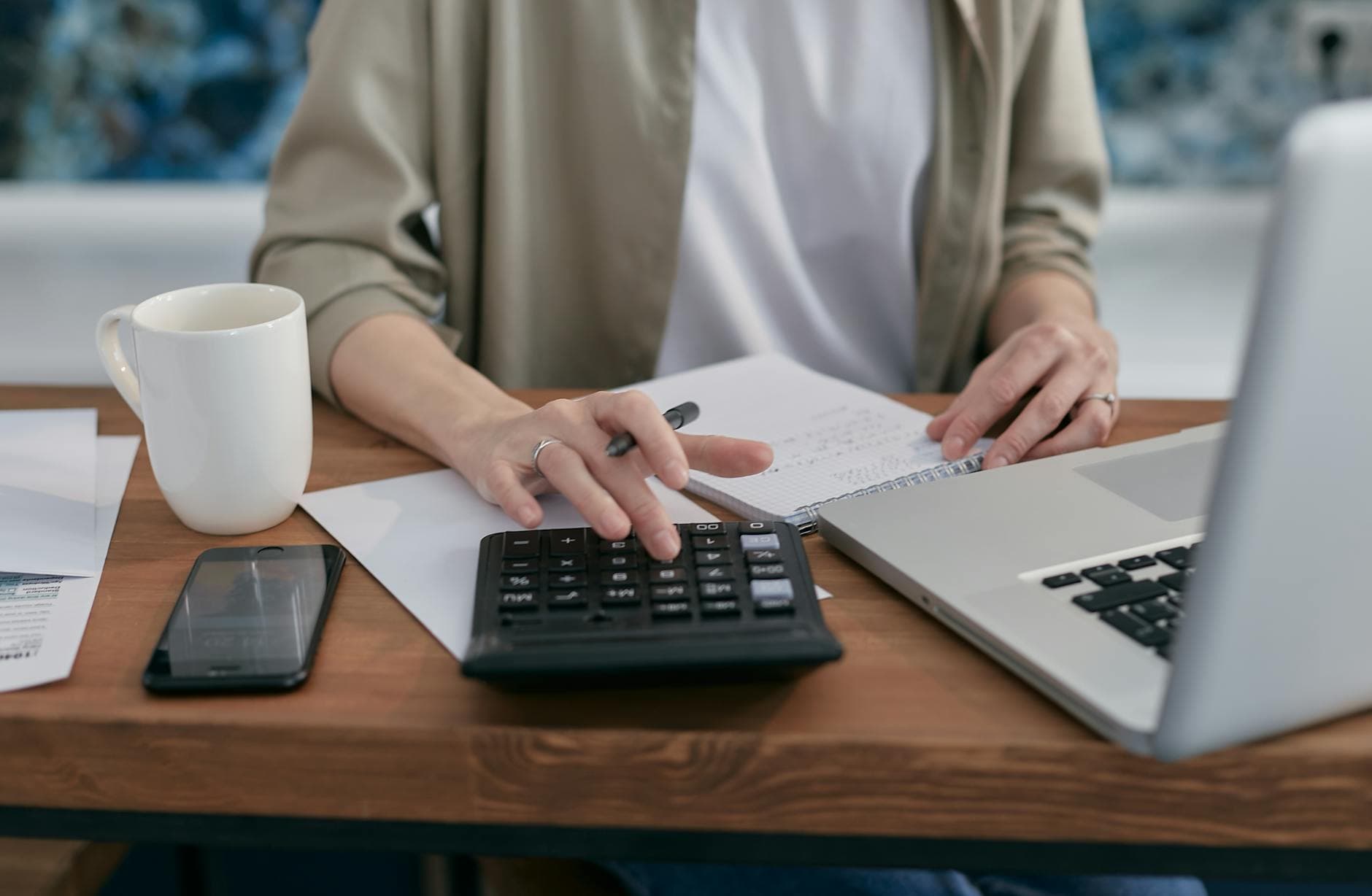 Self employed sole trader working on a laptop at a kitchen table with a calculator and tax documents nearby