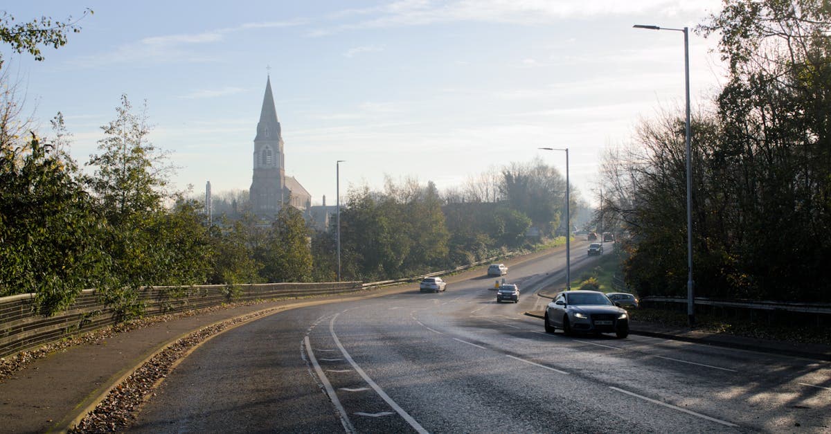 Cars drive along a peaceful road in Lisburn, Northern Ireland with a church in the background.