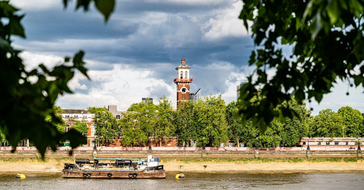 View of a historic London clock tower framed by lush trees along the riverbank.