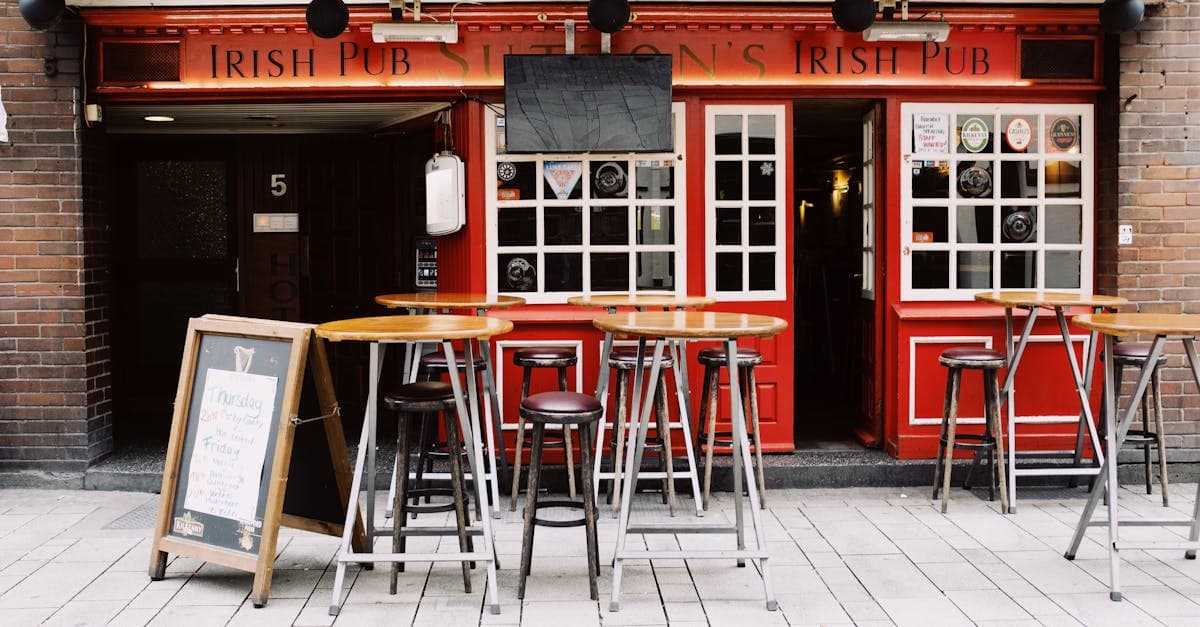 Empty terrace of local pub with empty tables and chairs against facade red window on sunny day in city
