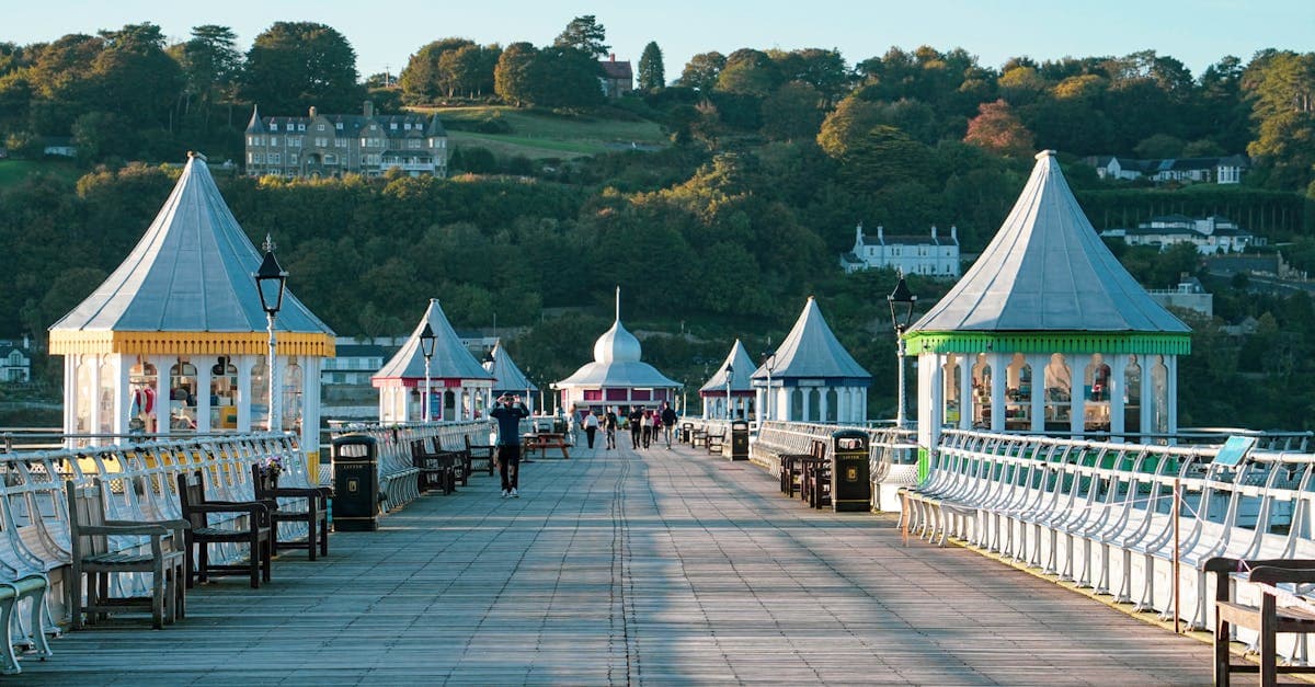 Charming view of Bangor Pier in Wales, showcasing vibrant kiosks and lush greenery.