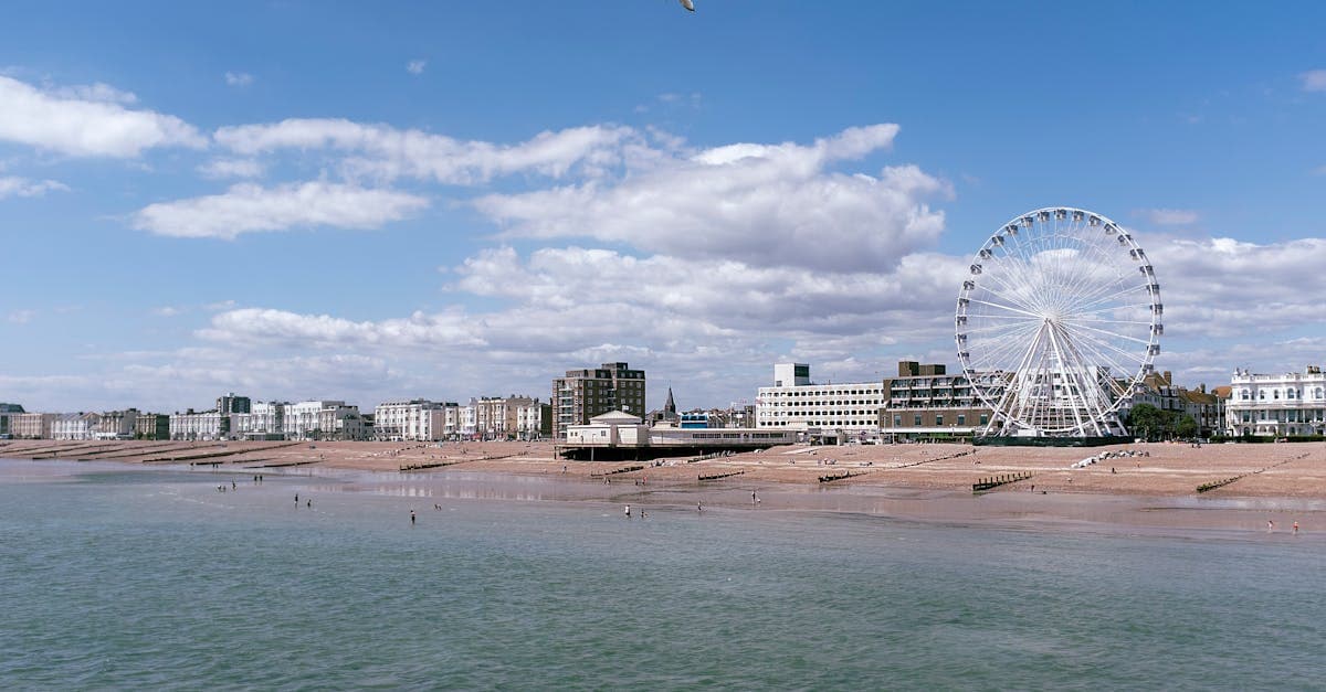 Scenic view of Worthing's seafront with a prominent observation wheel under a blue sky.