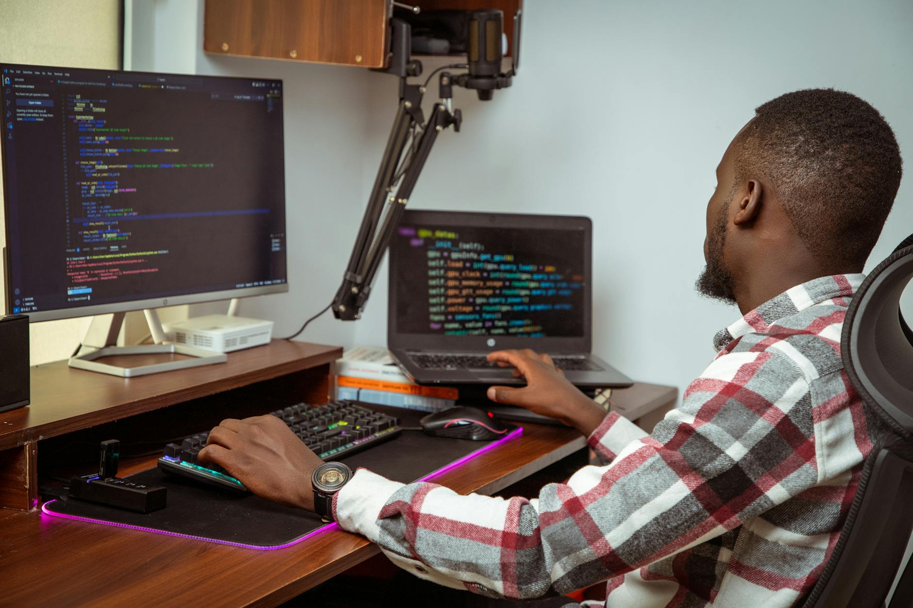 Software developer working on code at a desk in a modern UK office with dual monitors and notebooks